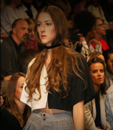 Model in a cropped cape and pleated skirt walking through the audience
