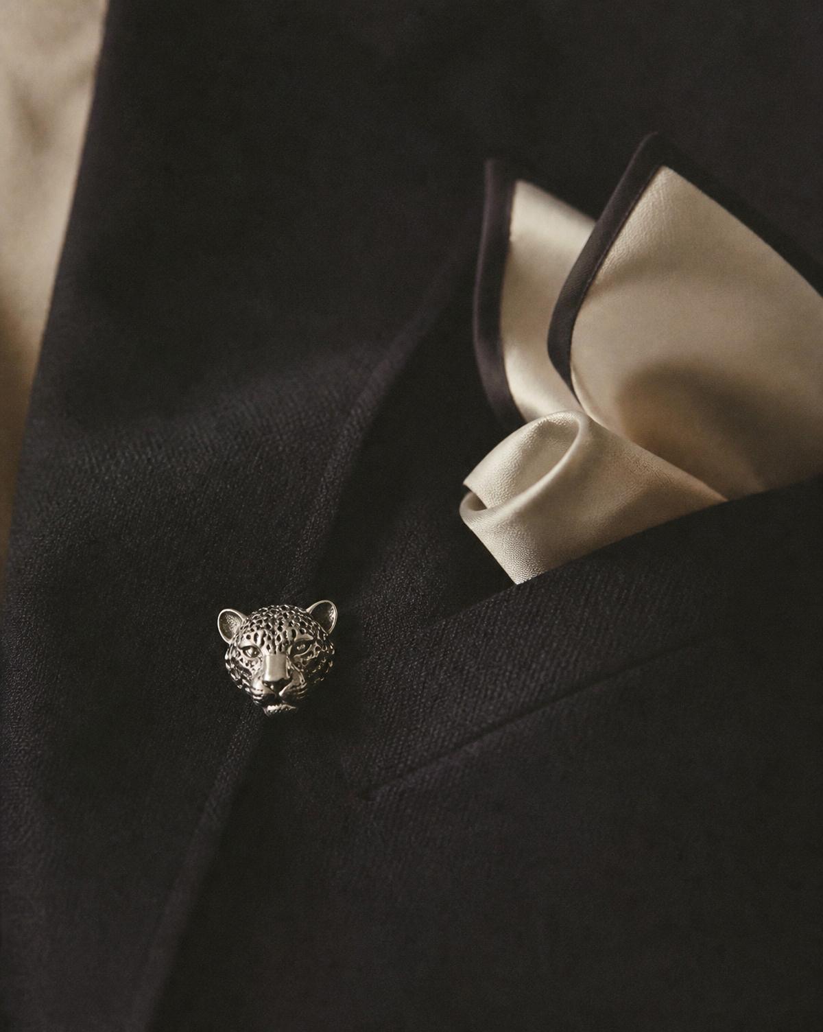 A silver leopard brooch on the lapel of a black wool jacket with an ivory silk pocket square